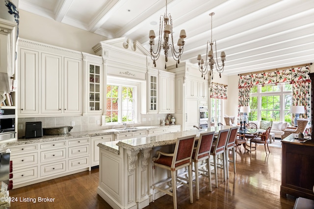 kitchen featuring an island with sink, backsplash, a breakfast bar, pendant lighting, and dark hardwood / wood-style flooring