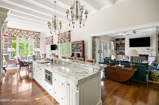 kitchen featuring an island with sink, light stone counters, decorative light fixtures, beam ceiling, and dark hardwood / wood-style floors