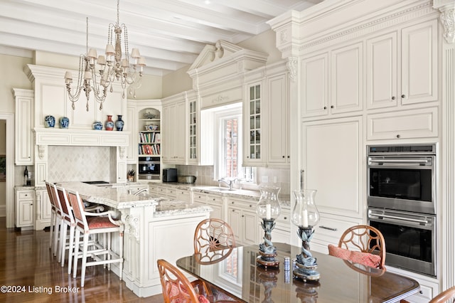 kitchen featuring decorative backsplash, beam ceiling, a kitchen island with sink, light stone countertops, and dark wood-type flooring