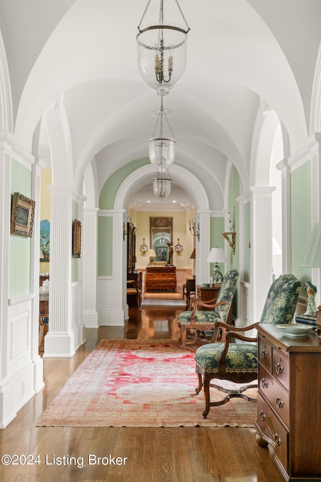 hallway with decorative columns, vaulted ceiling, a notable chandelier, and wood-type flooring