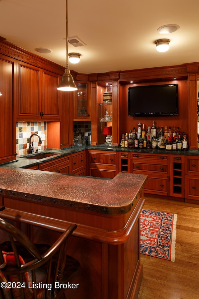 bar with sink, hanging light fixtures, light hardwood / wood-style floors, dark stone counters, and decorative backsplash