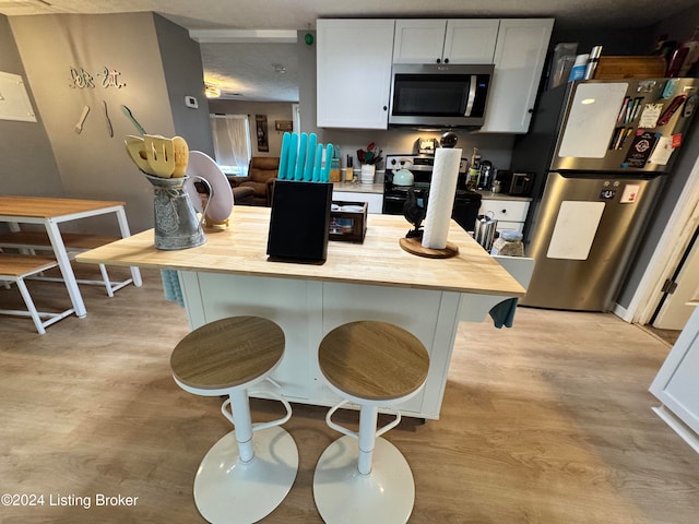 kitchen with white cabinetry, a kitchen bar, stainless steel appliances, and light wood-type flooring