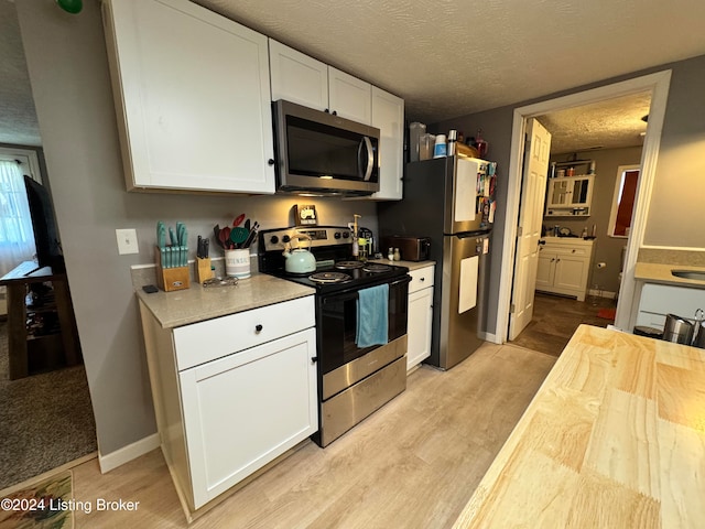 kitchen featuring white cabinetry, stainless steel appliances, a textured ceiling, and light hardwood / wood-style flooring