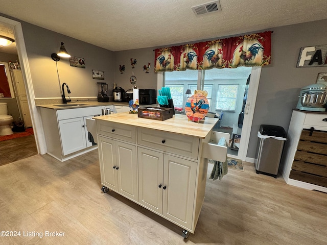 kitchen with sink, white cabinets, light wood-type flooring, butcher block countertops, and a textured ceiling