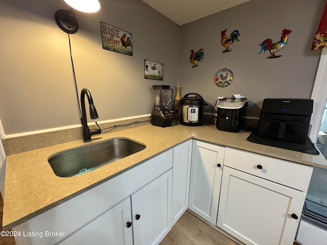 kitchen with light hardwood / wood-style flooring, kitchen peninsula, sink, white cabinetry, and a textured ceiling