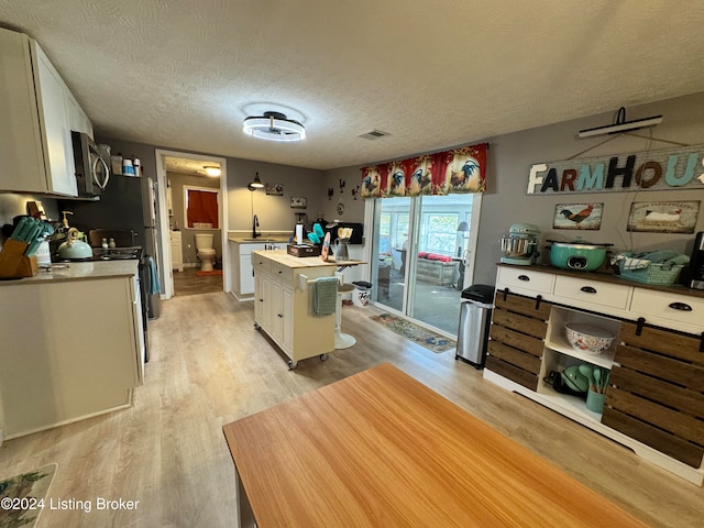 kitchen with white cabinetry, a textured ceiling, light wood-type flooring, and a kitchen island