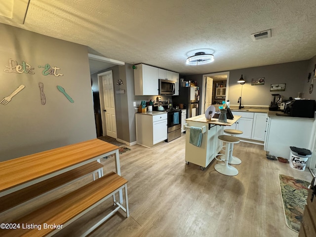 kitchen featuring stainless steel appliances, a textured ceiling, light wood-type flooring, and white cabinets