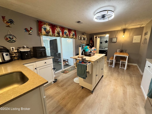 kitchen featuring sink, white cabinetry, a textured ceiling, and light wood-type flooring