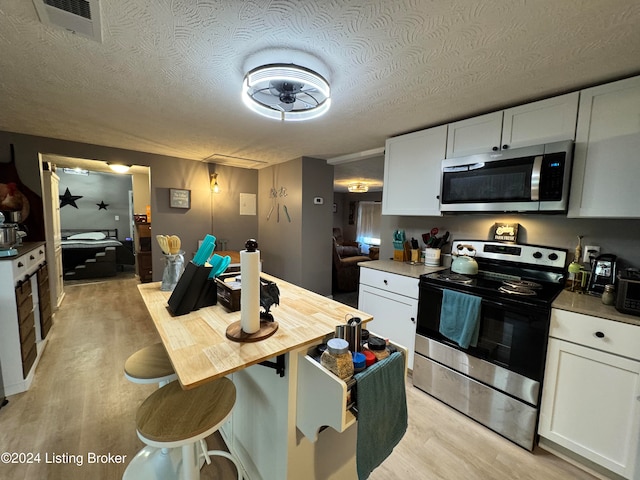 kitchen with appliances with stainless steel finishes, light wood-type flooring, a textured ceiling, white cabinetry, and ceiling fan