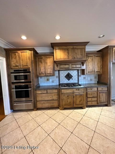 kitchen with tasteful backsplash, appliances with stainless steel finishes, premium range hood, ornamental molding, and light tile patterned flooring