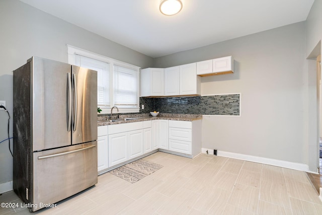 kitchen featuring white cabinets, tasteful backsplash, light stone countertops, stainless steel refrigerator, and sink