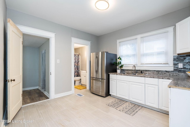 kitchen featuring white cabinetry, backsplash, stainless steel refrigerator, and sink