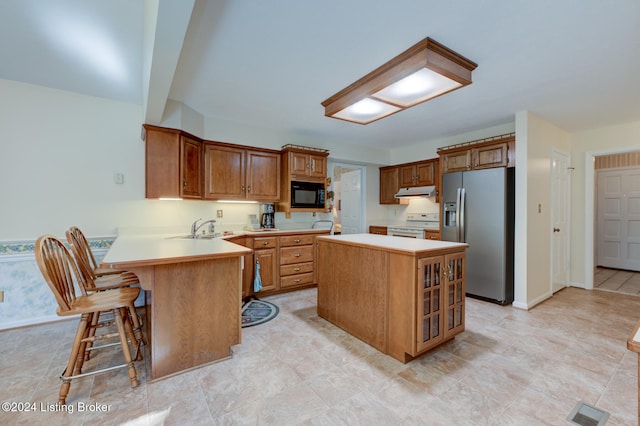 kitchen featuring white range, stainless steel refrigerator with ice dispenser, black microwave, kitchen peninsula, and a kitchen bar