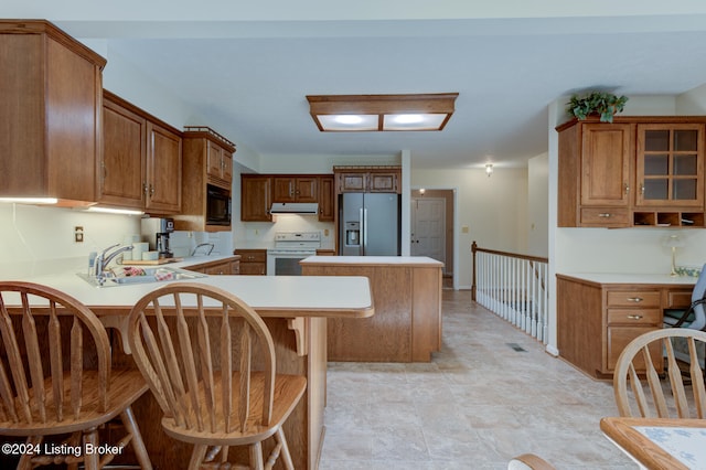 kitchen with white electric range, stainless steel refrigerator with ice dispenser, kitchen peninsula, sink, and a kitchen bar