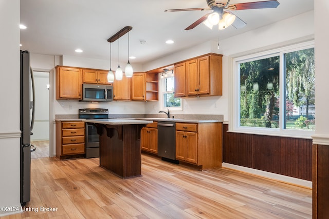 kitchen featuring a kitchen bar, light wood-type flooring, a kitchen island, hanging light fixtures, and stainless steel appliances