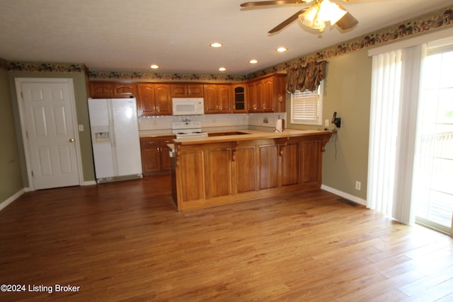 kitchen with kitchen peninsula, ceiling fan, a breakfast bar, light hardwood / wood-style floors, and white appliances