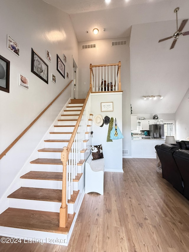 staircase featuring hardwood / wood-style flooring, high vaulted ceiling, and ceiling fan