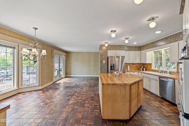 kitchen with butcher block countertops, white cabinetry, stainless steel appliances, a kitchen island, and decorative light fixtures