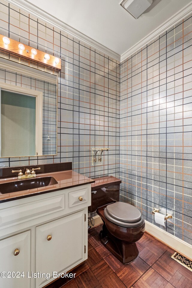 bathroom with tile walls, vanity, ornamental molding, parquet flooring, and toilet