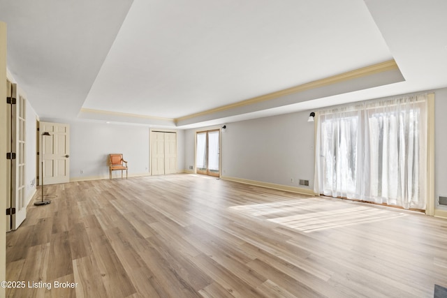 unfurnished living room with a raised ceiling, crown molding, and light hardwood / wood-style floors