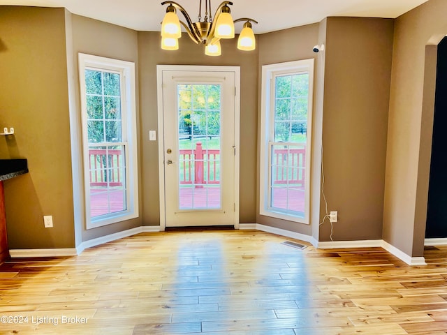 doorway to outside with light hardwood / wood-style flooring, a healthy amount of sunlight, and a notable chandelier