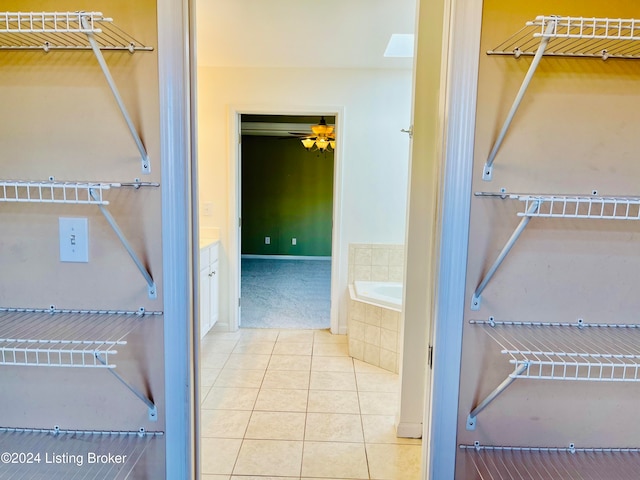 bathroom featuring tile patterned flooring, ceiling fan, a relaxing tiled tub, vanity, and a skylight