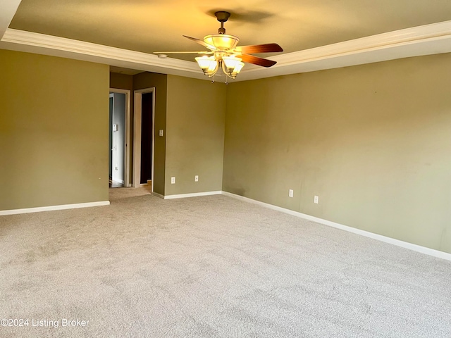 empty room with ceiling fan, a raised ceiling, carpet flooring, and crown molding