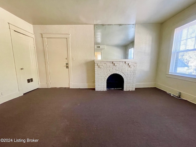 unfurnished living room with dark colored carpet and a brick fireplace