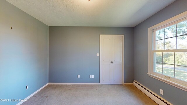 interior space featuring baseboards, light colored carpet, a closet, a textured ceiling, and a baseboard radiator