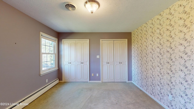 unfurnished bedroom with visible vents, two closets, a baseboard heating unit, carpet flooring, and a textured ceiling