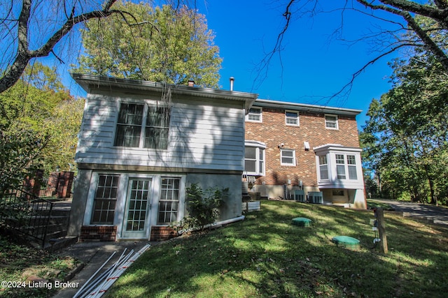 rear view of house featuring central AC unit, a lawn, and brick siding