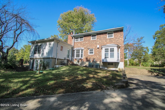 rear view of property with brick siding, central air condition unit, a lawn, and a chimney