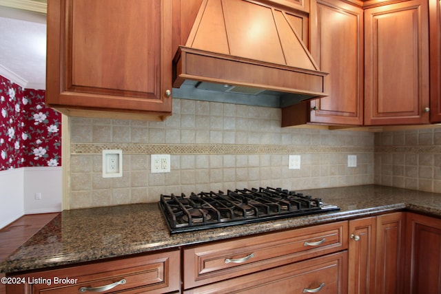 kitchen with brown cabinets, black gas cooktop, custom range hood, and dark stone countertops