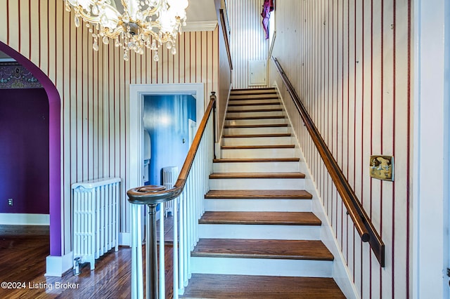 stairs with wood-type flooring, an inviting chandelier, and wood walls