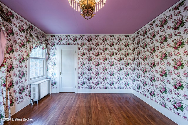 spare room with a notable chandelier, dark hardwood / wood-style floors, and radiator heating unit