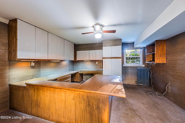 kitchen with kitchen peninsula, radiator heating unit, white cabinets, and carpet floors