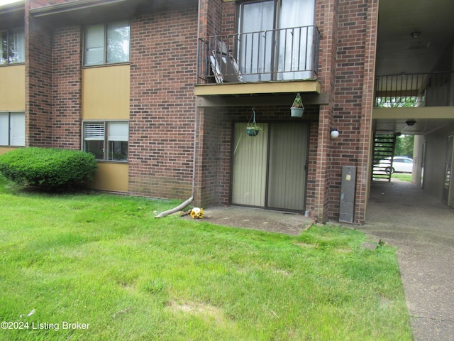 view of exterior entry with a balcony and a yard