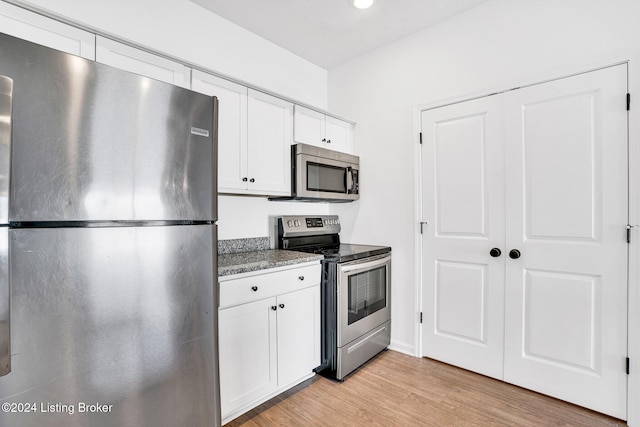 kitchen featuring white cabinetry, light hardwood / wood-style floors, stainless steel appliances, and dark stone counters