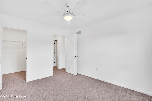 unfurnished bedroom with a closet, ceiling fan, carpet flooring, and a walk in closet