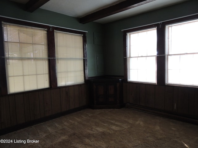 spare room featuring beamed ceiling, a baseboard radiator, dark carpet, and wooden walls