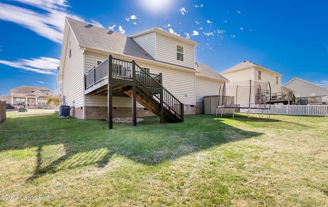 rear view of property with a yard, a trampoline, a deck, and central air condition unit