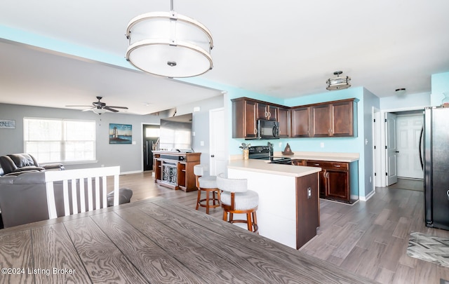 kitchen with black appliances, hardwood / wood-style floors, ceiling fan, dark brown cabinetry, and a breakfast bar area