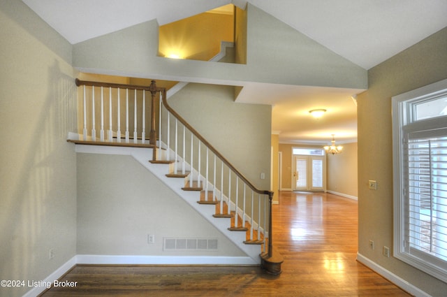 stairs featuring a chandelier, a healthy amount of sunlight, vaulted ceiling, and hardwood / wood-style flooring