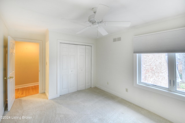 unfurnished bedroom with ceiling fan, light colored carpet, crown molding, and a closet