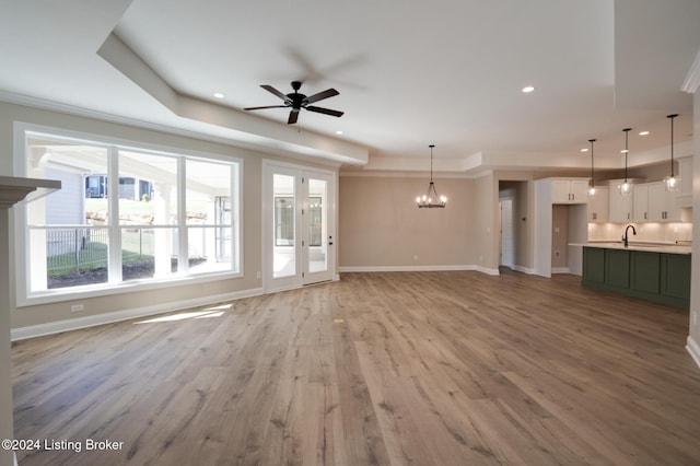 unfurnished living room featuring ceiling fan with notable chandelier, light wood-type flooring, and sink