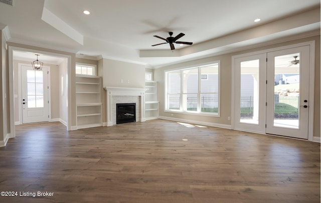 unfurnished living room featuring a tiled fireplace, dark hardwood / wood-style flooring, ceiling fan with notable chandelier, and ornamental molding