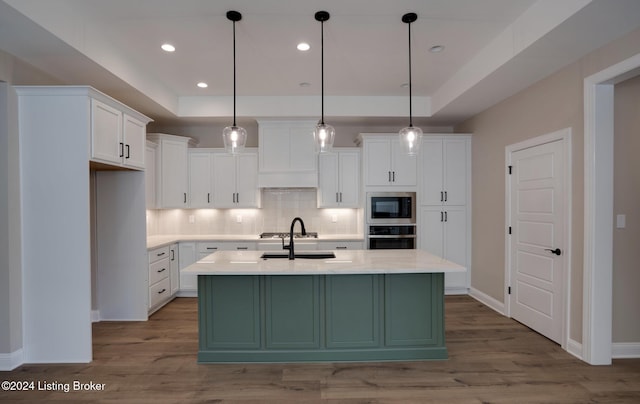 kitchen with light hardwood / wood-style flooring, stainless steel appliances, hanging light fixtures, and an island with sink