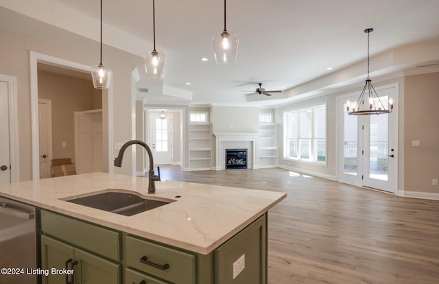 kitchen featuring light stone countertops, hanging light fixtures, green cabinetry, an island with sink, and light wood-type flooring