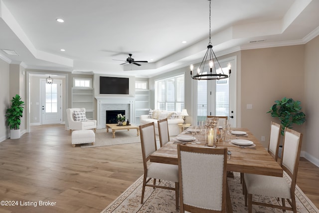 dining space featuring ceiling fan with notable chandelier, crown molding, a tray ceiling, and light hardwood / wood-style flooring