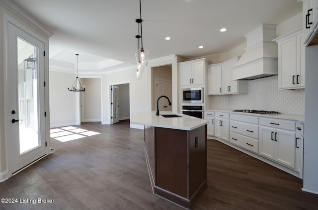 kitchen with custom range hood, an island with sink, hanging light fixtures, and plenty of natural light